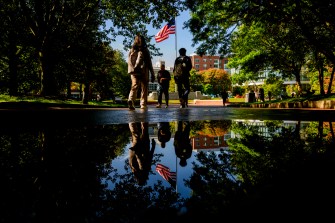 People walking on a path reflected in a puddle on a sunny day.