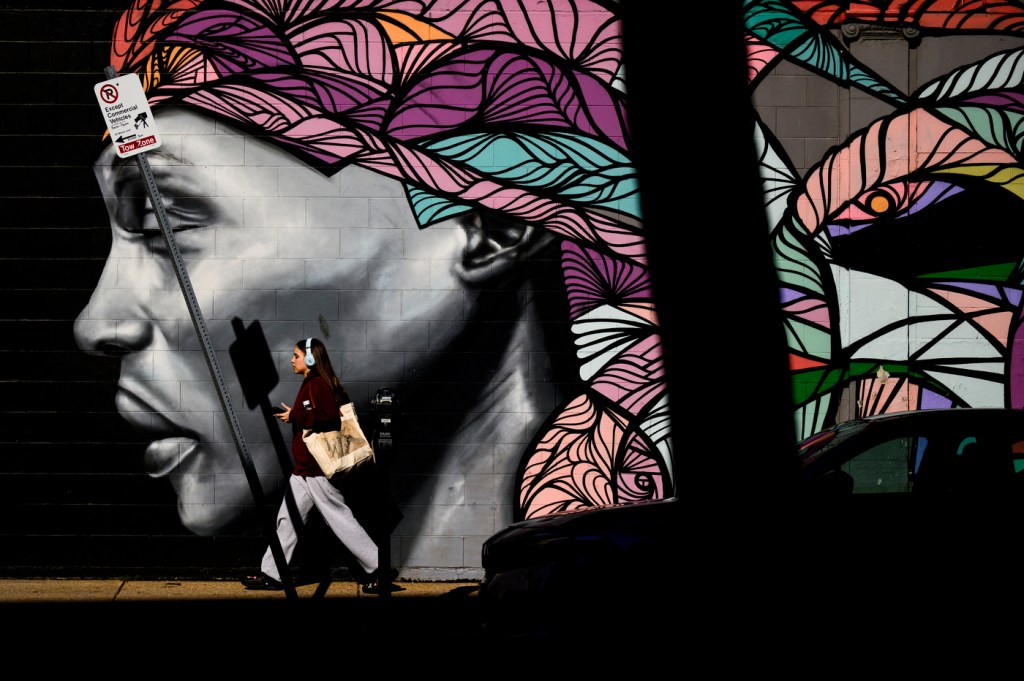 A person walks in the morning light past a vibrant multi-colored mural.