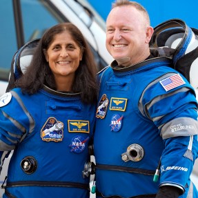 Astronauts Suni Williams and Butch Wilmore standing arm in arm smiling.