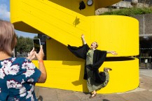 A family member taking a photo of a graduate throwing their cap in the air outside.