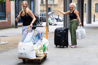 On a sunny day, two people move bags, bins, and luggage into residence halls.