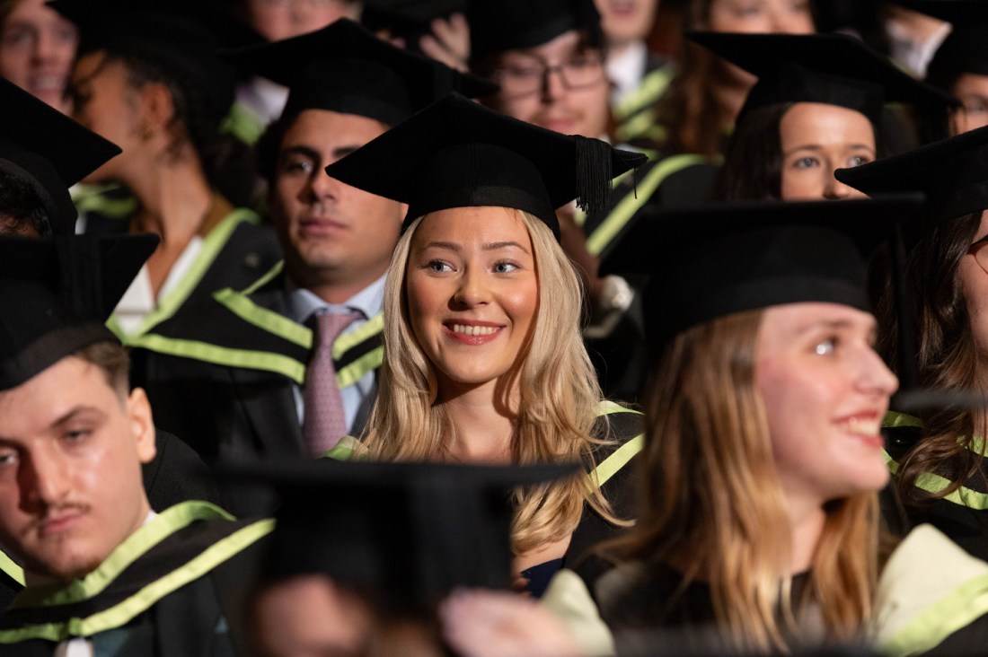 A graduate sitting amongst their peers smiling.