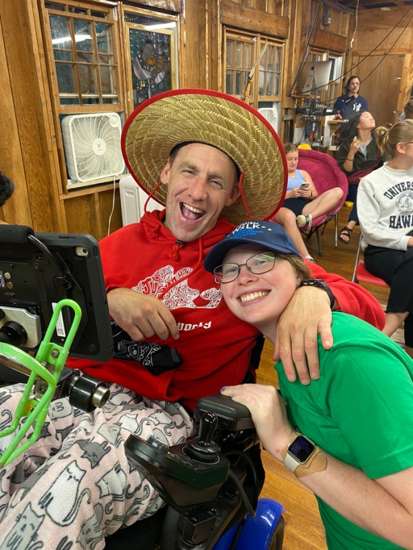 A student and a person with disabilities wearing a straw hat posing together.