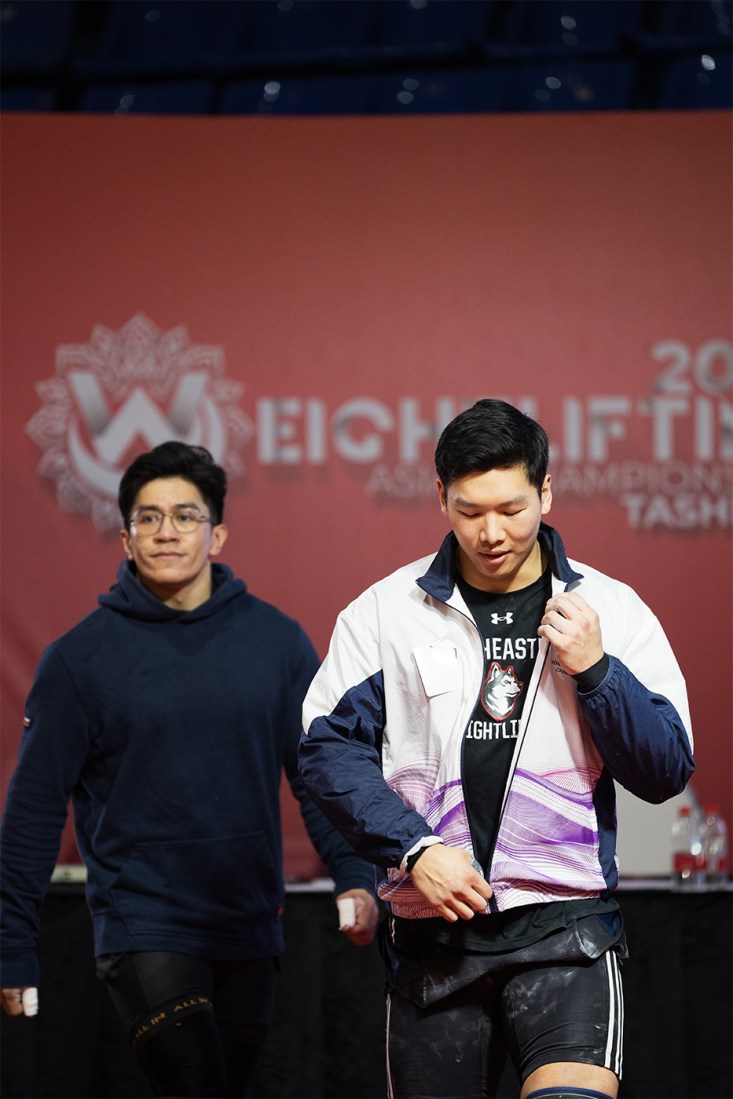 Matthew Tung unzipping his jacket at a weightlifting competition.