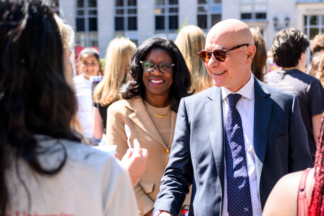 Dayna Matthew and President Joseph E. Aoun walk around Northeastern's campus while shaking hands with people.