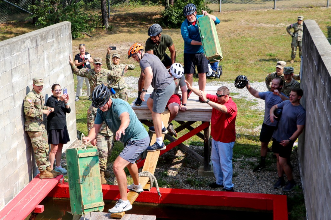 Students balanced on wooden beams crossing over a pool of water.