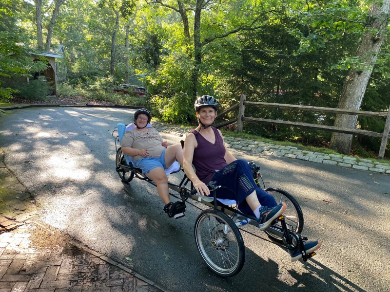 Kim Ho riding a two-person tandem bicycle along with a person with a disability. 