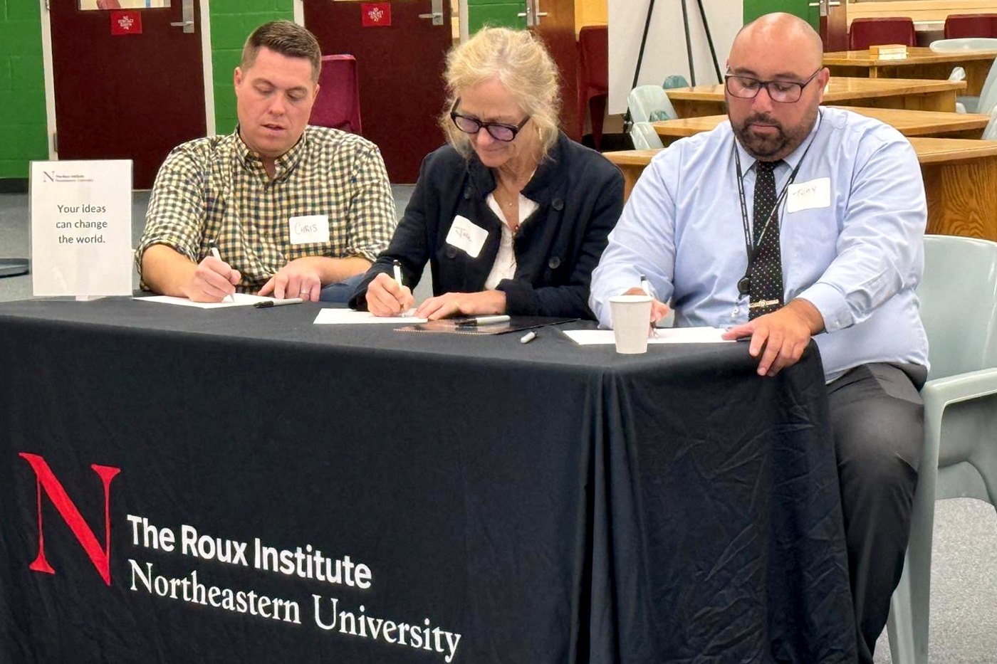 Three judges sitting at a table covered in a black tablecloth with the Northeastern Roux Institute logo on it. 