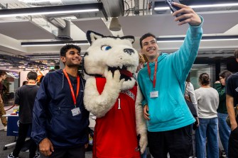 Two people pose for a picture with a husky-themed mascot.