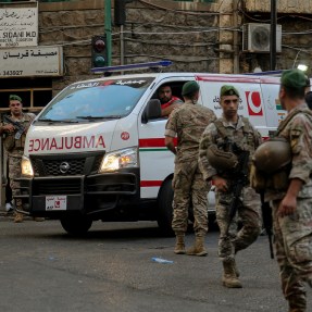 Lebanese army soldiers standing in the street while an ambulance drives by.