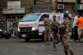 Lebanese army soldiers standing in the street while an ambulance drives by.