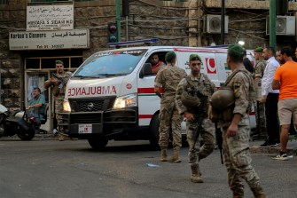 Lebanese army soldiers standing in the street while an ambulance drives by.