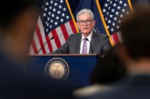 Jerome Powell speaking at a podium in front of two US flags.