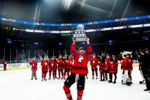 Skylar Irving standing on the ice holding the Beanpot trophy over her head.