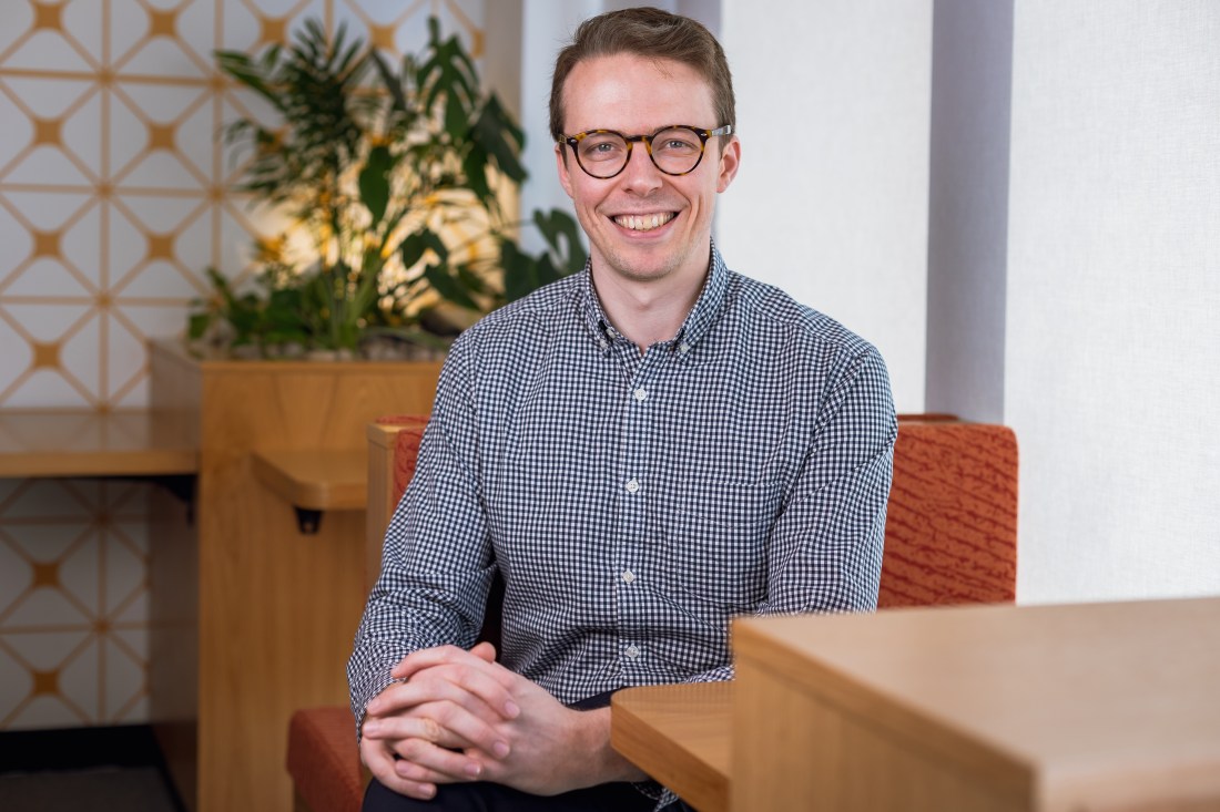 Headshot of Tomas Elliott wearing a checked shirt and smiling.