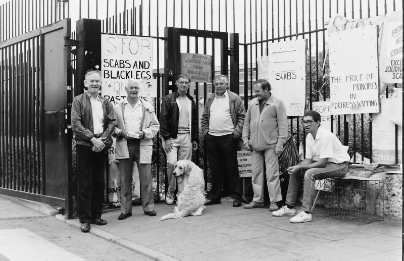 A black and white photo of a group of people standing in front of protest signs with a dog.