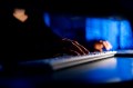 Close-up of a person's hands typing on a keyboard in a dimly lit room.