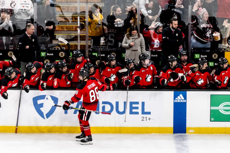 A womans hockey player skating next to the bench high fiving her team mates.