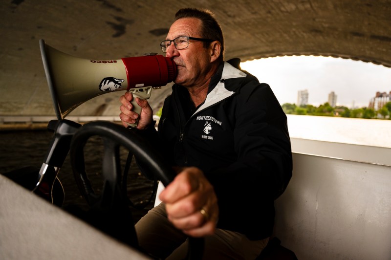 A person speaks into a blowhorn while traveling down a river on a boat.