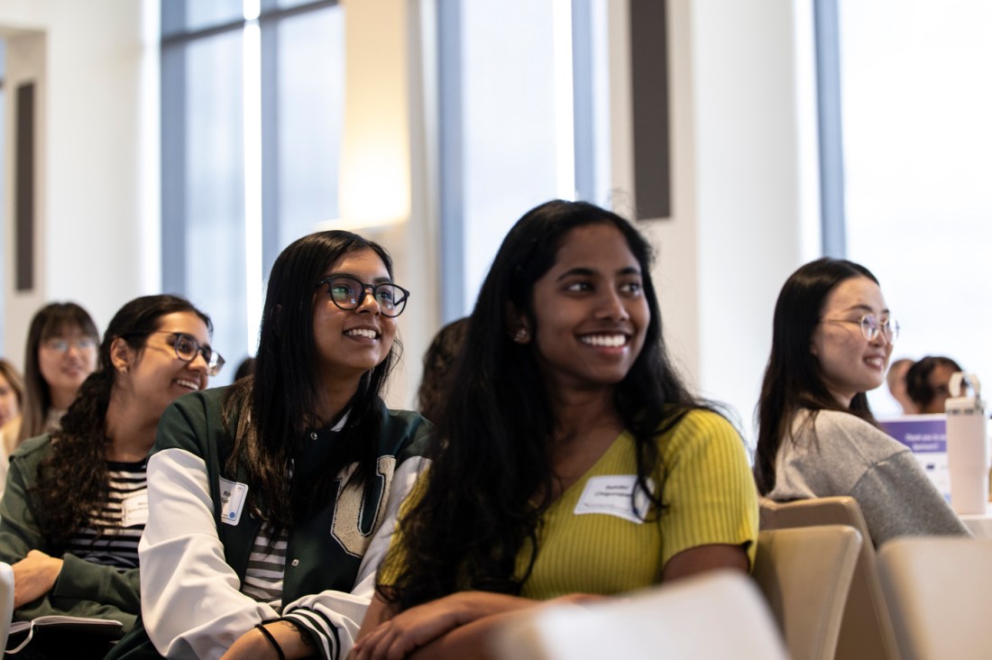 An audience of students and professionals smiling and listening during a presentation at the Women of the Cloud College Tour.