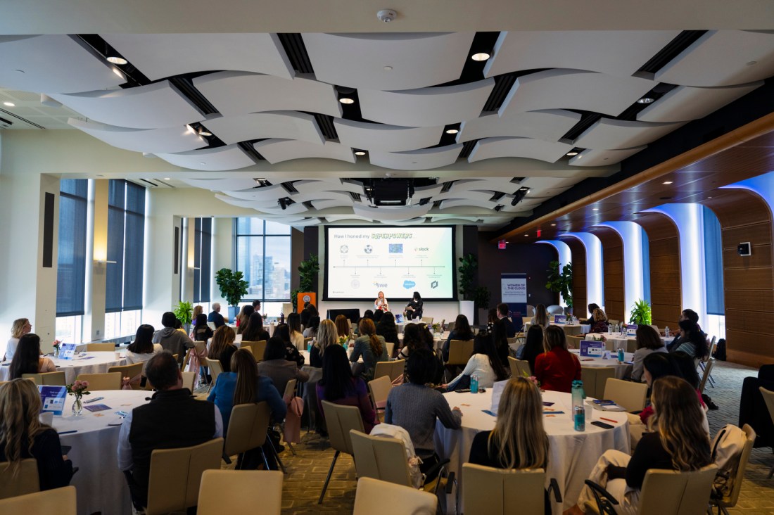 An audience of students and professionals smiling and listening during a presentation at the Women of the Cloud College Tour.