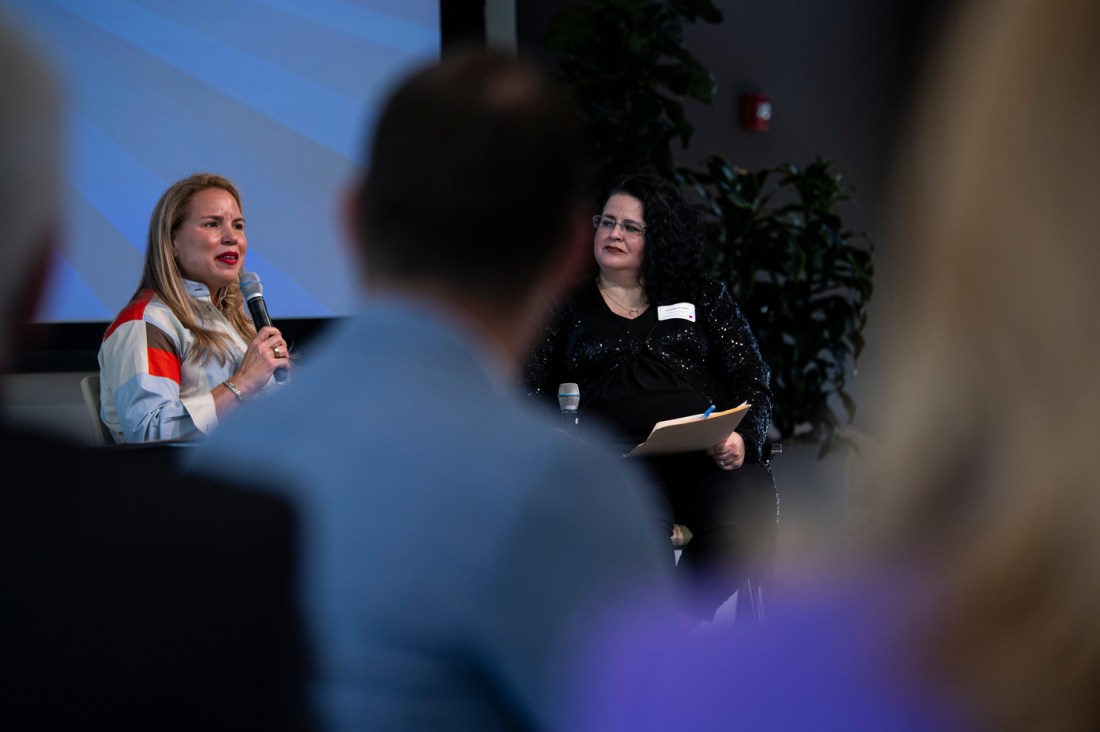 A woman speaking at a tech event with a group of attendees listening in a modern venue.