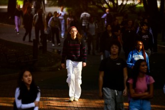 Dozens of people walk through a campus on a sunny day.