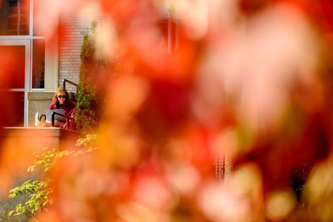 A student standing outside Richards Hall, framed by fall foliage.