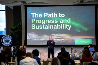 A person stands on a stage before a PowerPoint presentation titled "The Path to Progress and Sustainability".