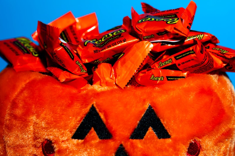 A stuffed orange pumpkin with a pile of Reese's Peanut Butter Cups on top.