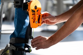 A person adjusting an exoskeleton on a person's leg.