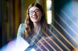 Laurel Gabard-Durnam is smiling with her hands clasped while seated for a portrait. She has brown hair and glasses.