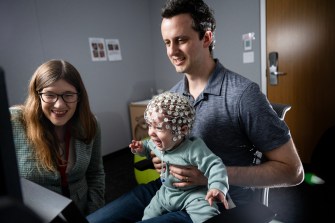 A person holding a baby with a neuroimaging cap on.