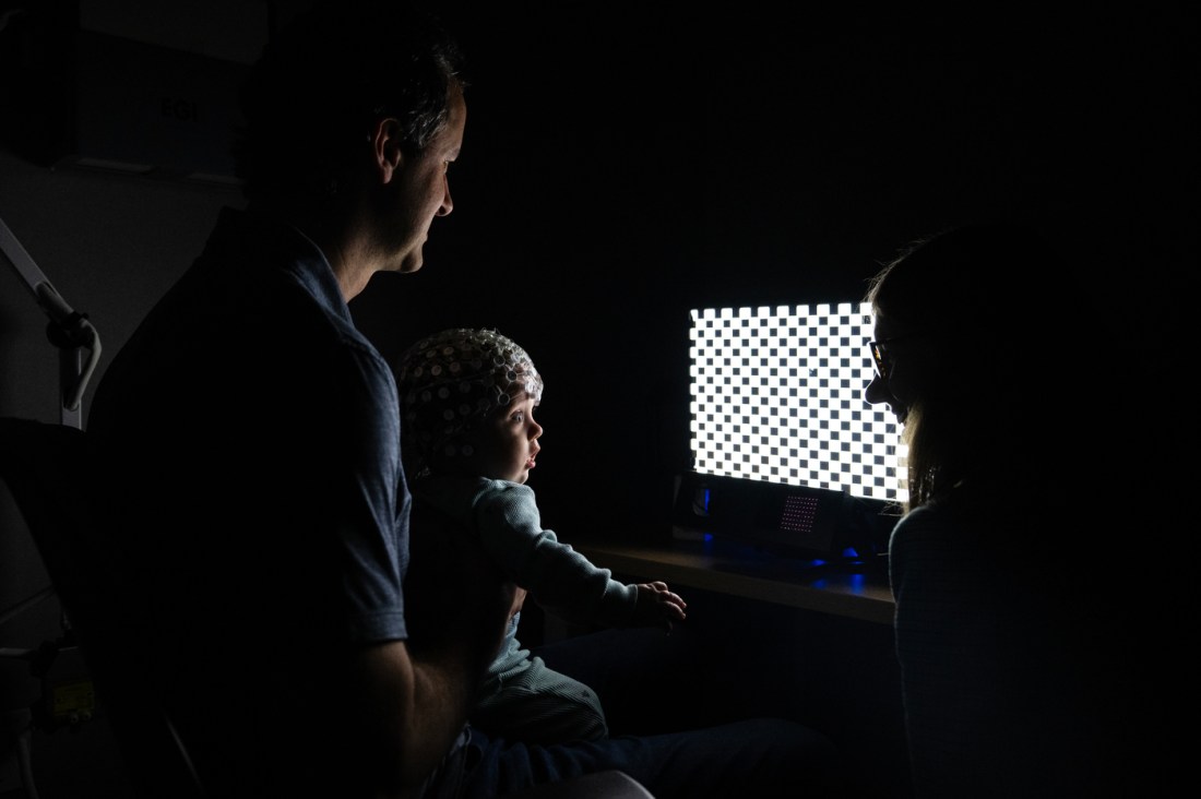 Laurel Gabard-Durnam and David Martin in a dark room in front of a screen with their baby Reid Martin.