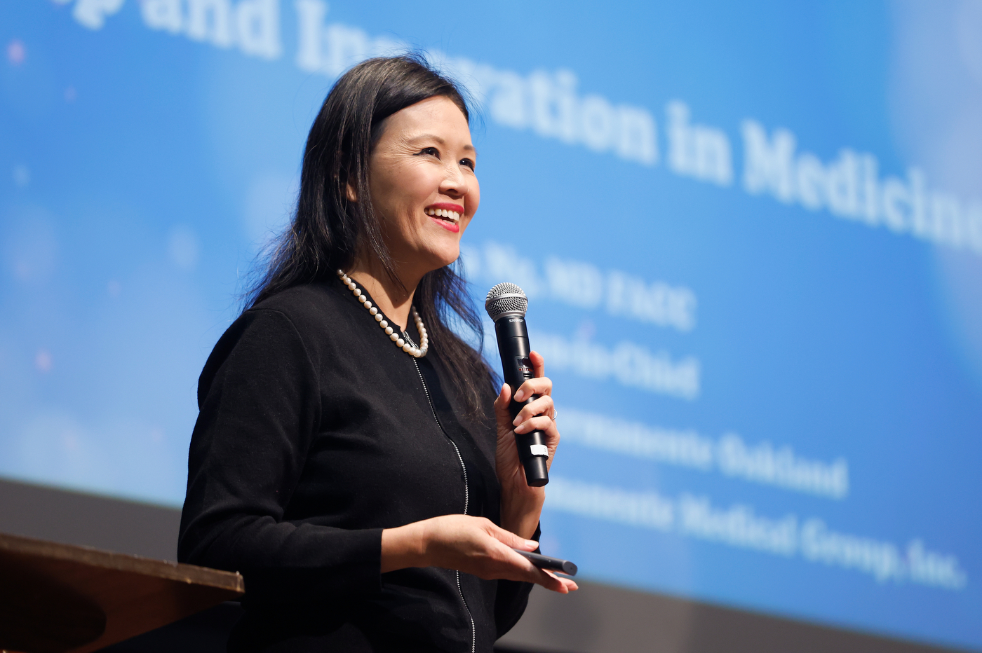 Dr. Rita Ng holding a microphone and smiling.