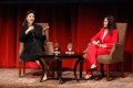 Dr. Rita Ng speaking into a microphone and gesturing with one hand while sitting on a stage in a lecture hall on the Oakland campus.