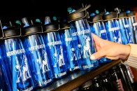 A person's hand picking up a Northeastern branded reusable water bottle from a shelf of them.