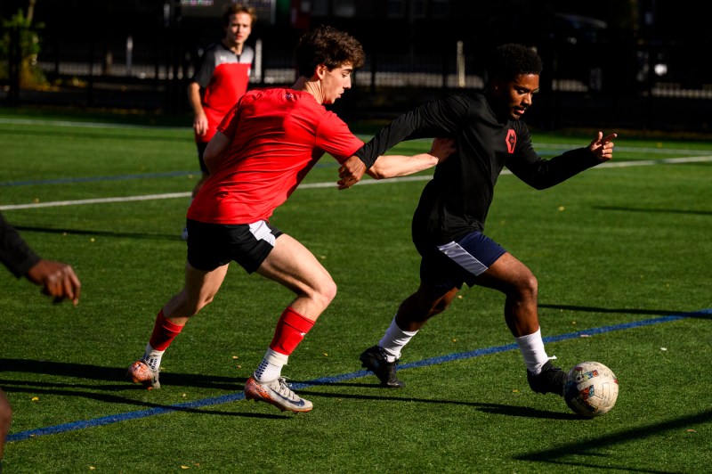 A soccer player dribbling with the ball away from another player.