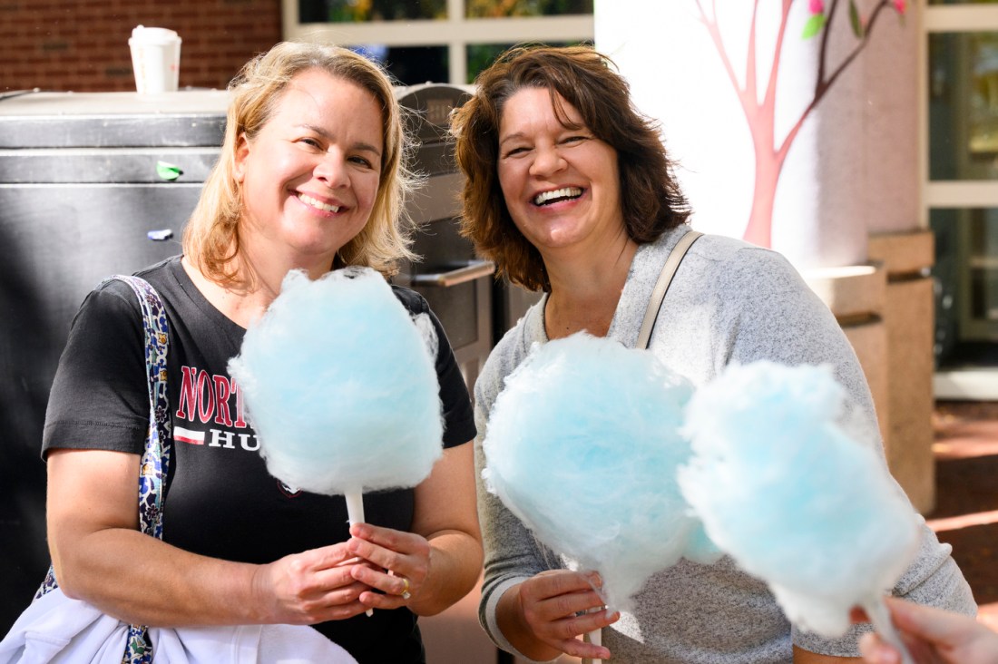 Two people posing together with sticks of blue cotton candy. 