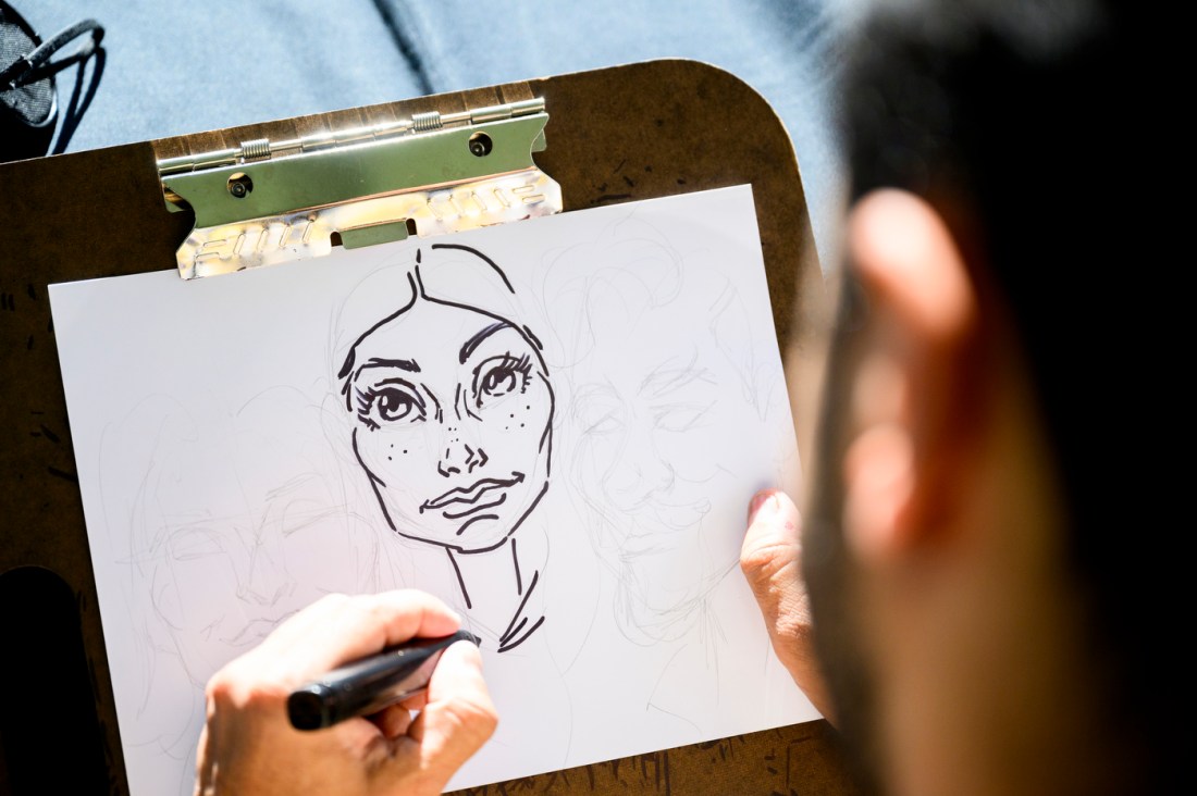 A person drawing a sketch of another person using white paper and a marker. 