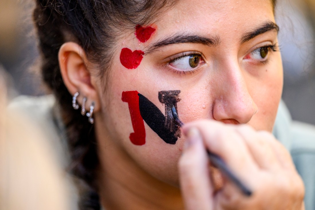 A person getting their face painted with a red and black 'N' for Northeastern.