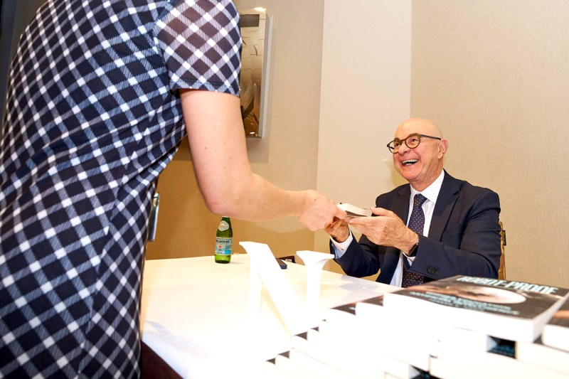 President Aoun smiling while handing a signed copy of his book to another person.