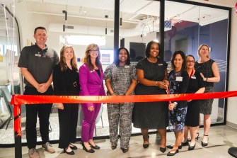 A group of people standing in front of a large red ribbon at the Charlotte campus.