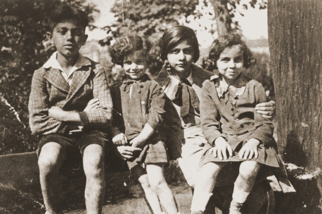 An old photo of four children sitting on a tree branch.