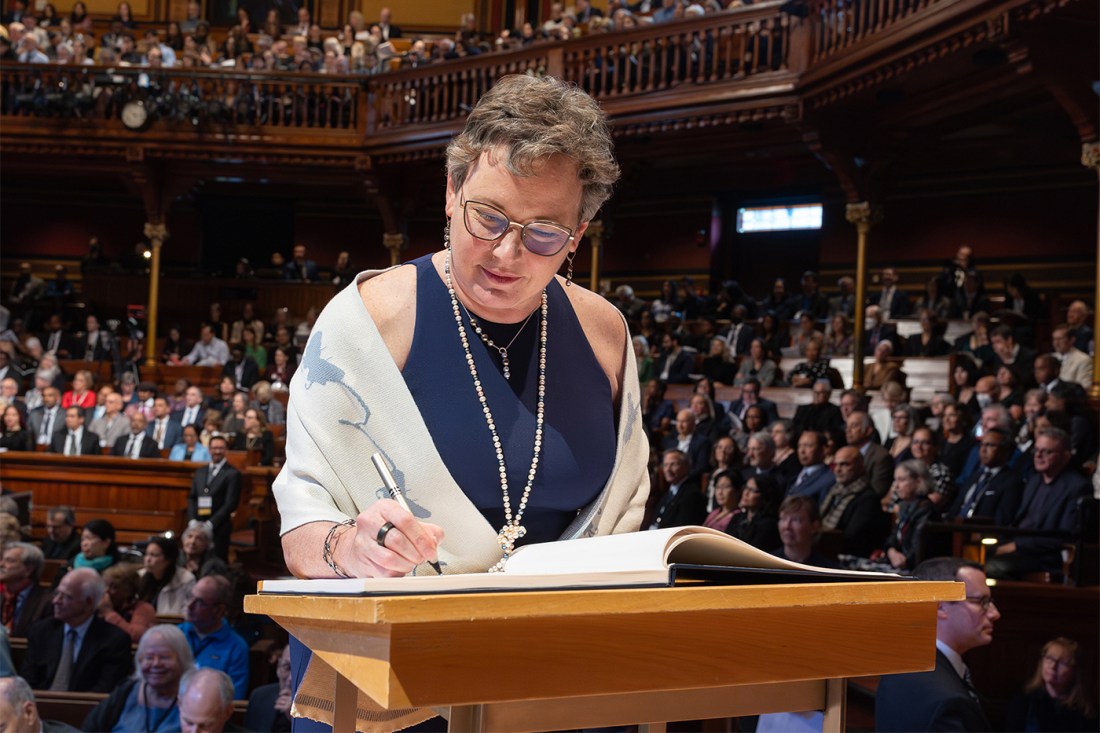 Dean Beth Mynatt wearing a white shawl with blue butterflies on it while signing a large book in front of a crowd. 