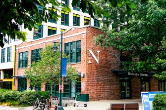 A brick building in Seattle surrounded by green trees and bushes. It has a white 'N' logo on it for Northeastern.