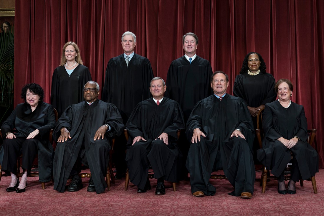 Group photo of the U.S. Supreme Court justices sitting and standing before a red curtain.