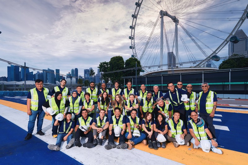 A team of people wearing yellow vests posing on the track of the Singapore Grand Prix in front of a ferris wheel.