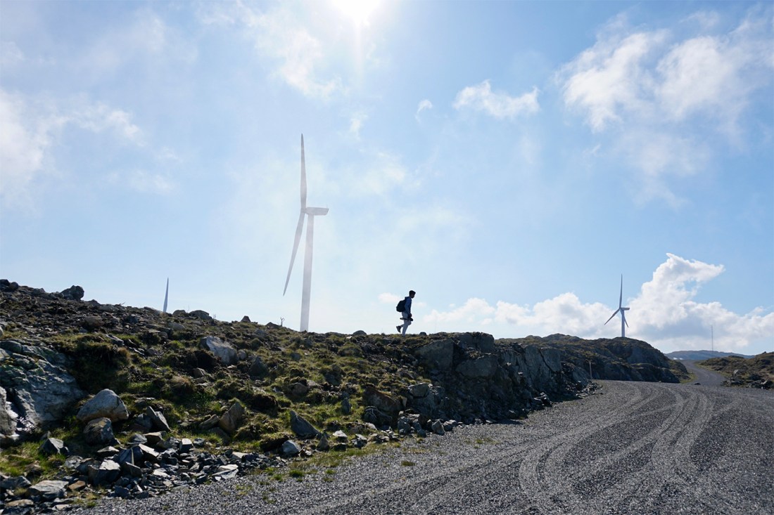 The silhouette of a student walking on the ridge of a hill, a wind turbine in the background.