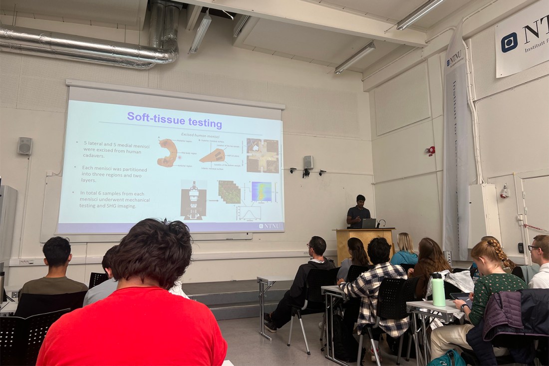 A room full of students listening to a person teaching at the front of the room. There is a slide being projected with the headline 'Soft-tissue testing' that has several bullet points of text and six diagrams. 